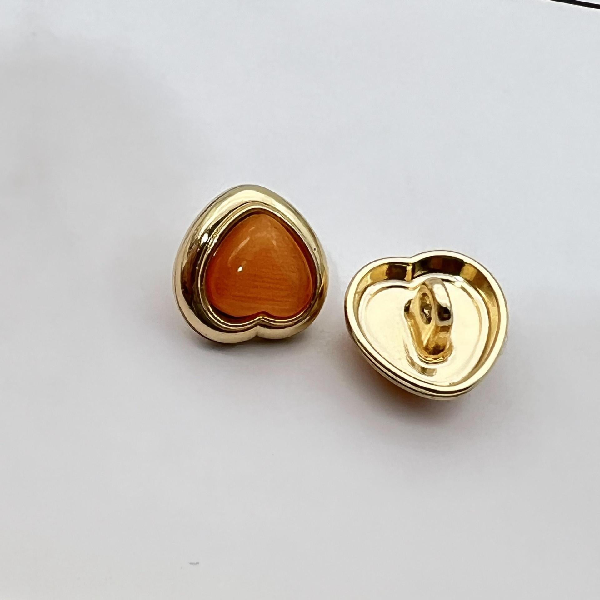 Heart-shaped pearlized resin button, amber-orange center with gold metal shank and back
