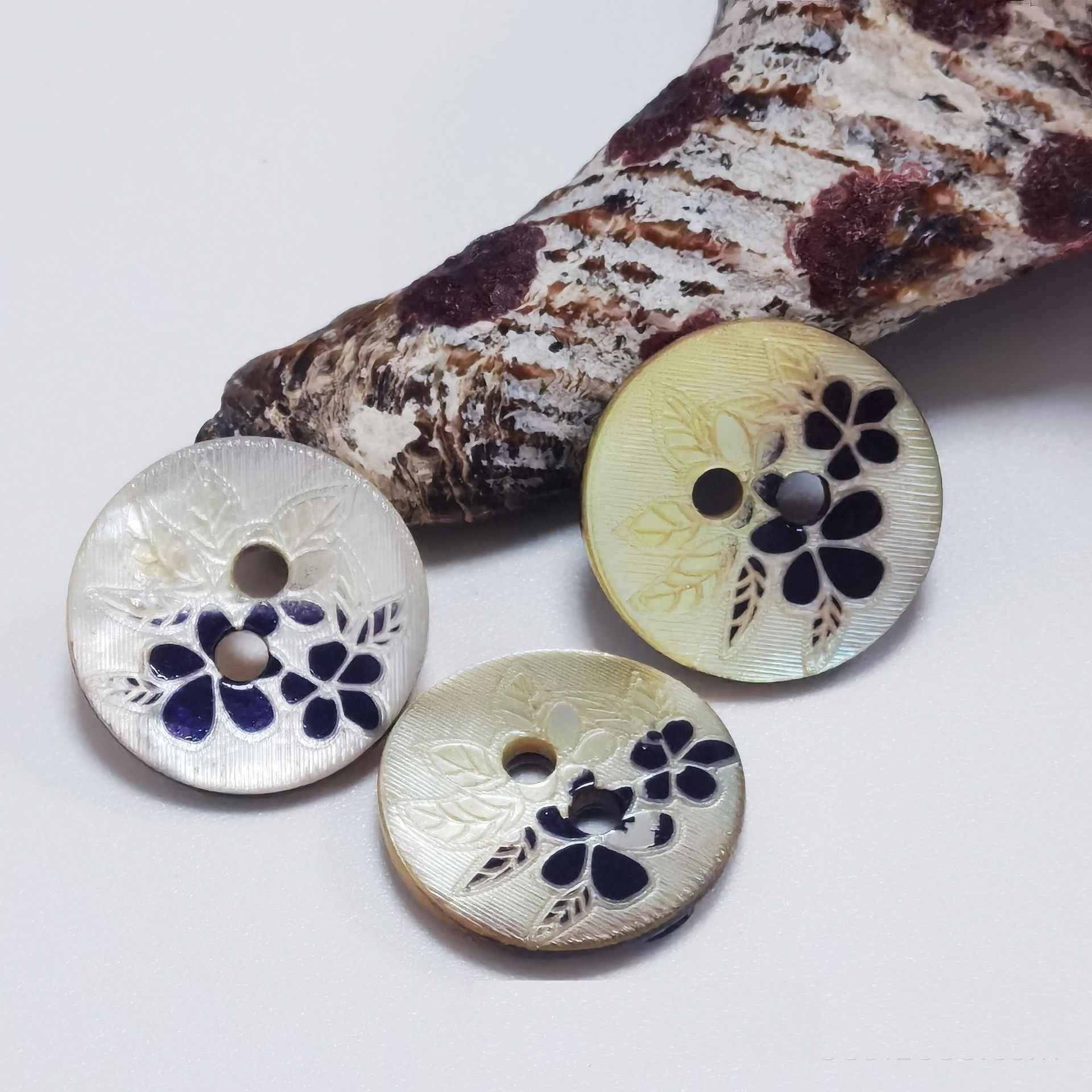 Three mother-of-pearl 2-hole buttons with flower cutout in navy on light shells, round, 2 holes.