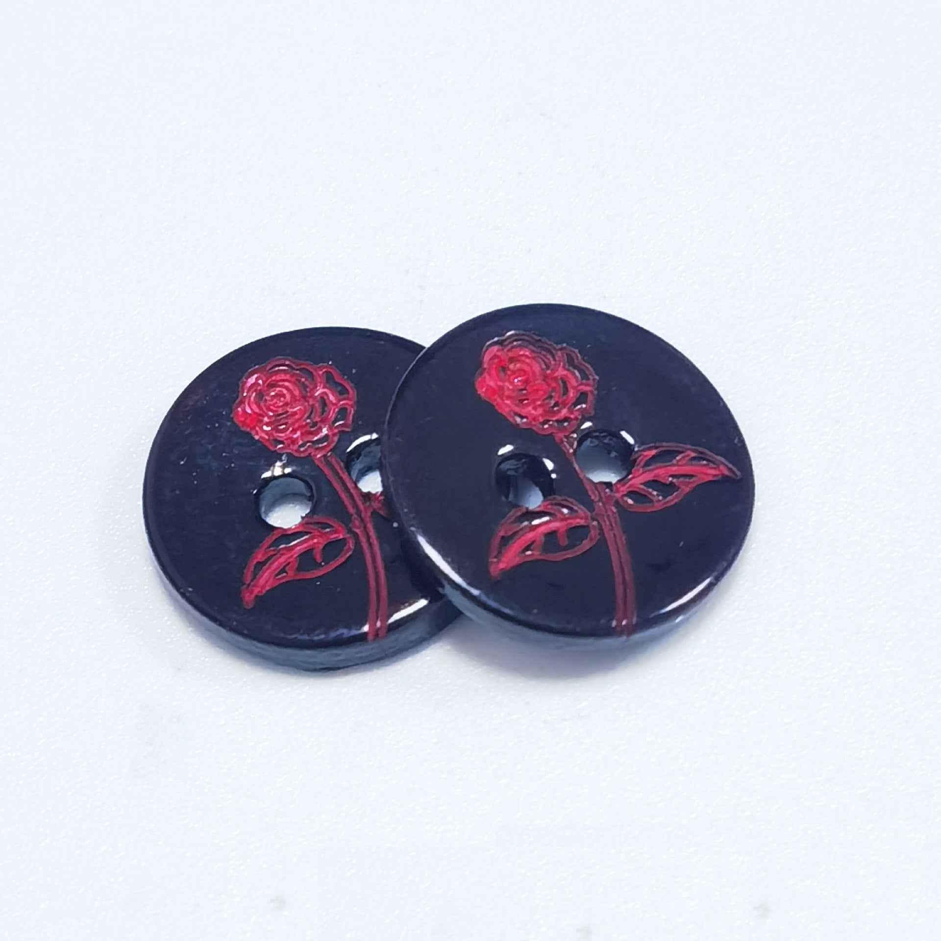 Close-up of glossy black round buttons with red rose vine floral print and visible holes