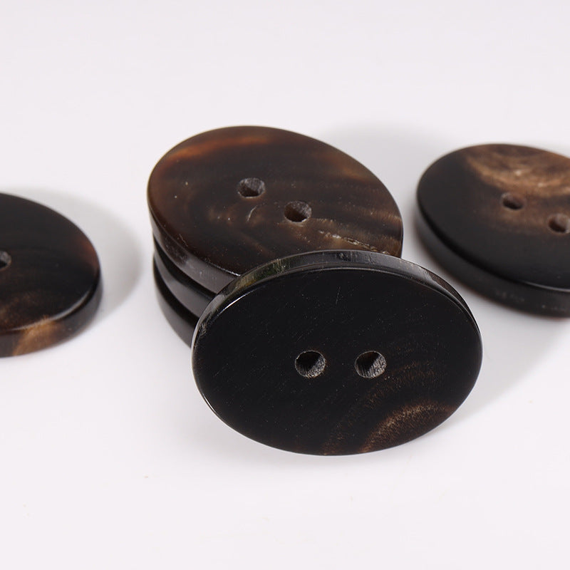Oval 23mm two-hole horn buttons in dark coffee; close-up view of front faces.