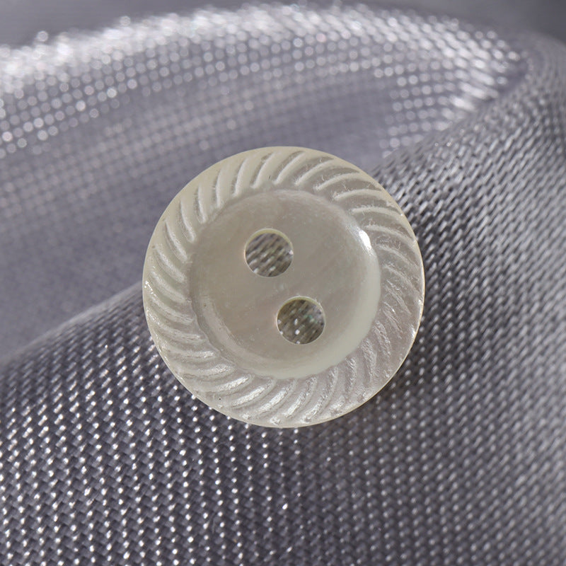White two-hole shell button, wide-edge ridged rim, close-up of two holes