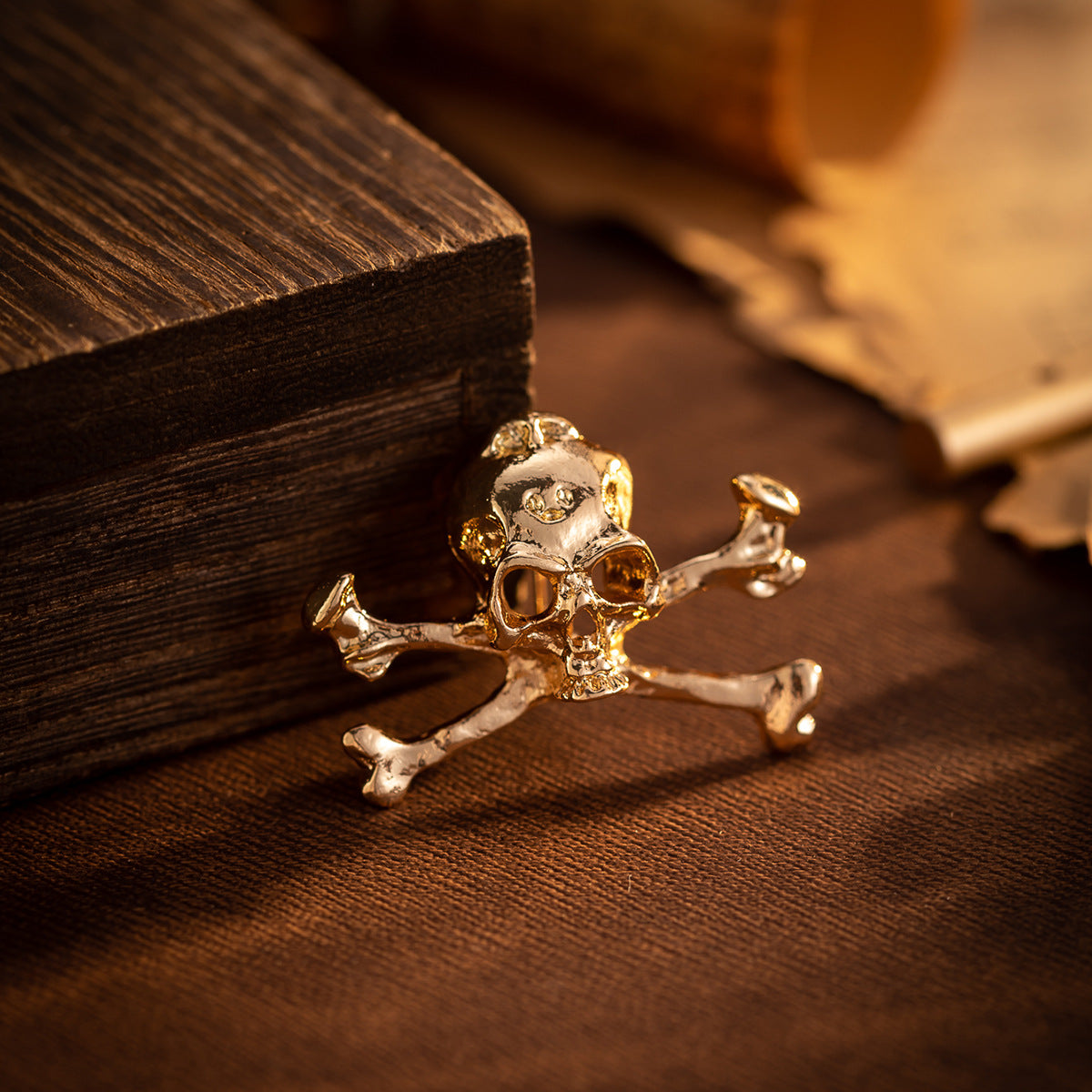 Gold skull crossbones metal brooch pin, front view on dark wooden background