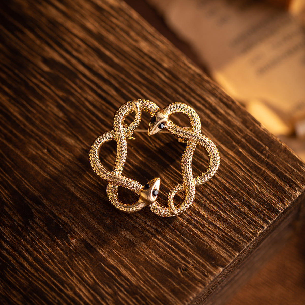 Gold flower-and-snake metal brooch with textured coiled loops and black enamel eyes