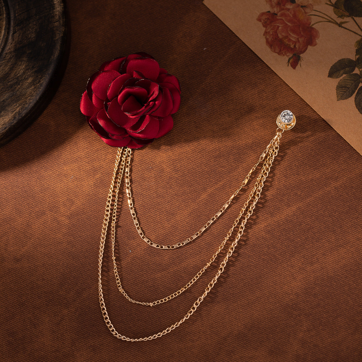 Weinrote Blumenbrosche mit goldfarbener Kette und runder Strassnadel
