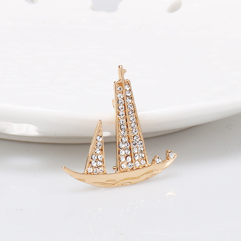 Gold-tone sailboat lapel pin brooch with rhinestone sails and wave base