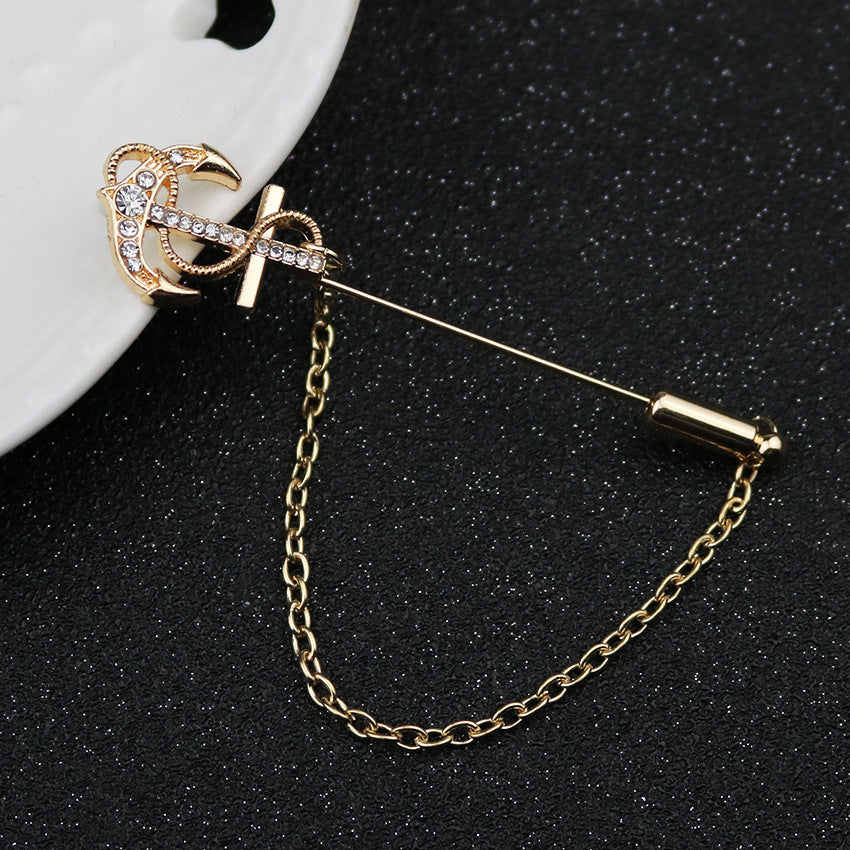 Gold-tone long-pin lapel brooch with anchor-and-rhinestone design, linked chain