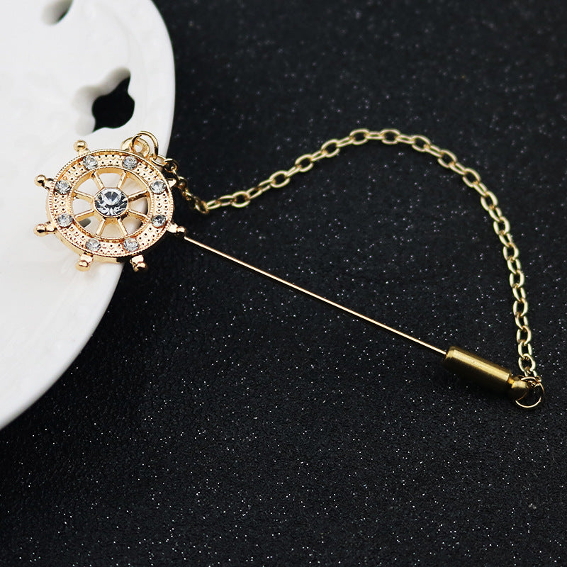 Ship-wheel long-pin lapel brooch with rhinestone rim and linked chain, gold-tone