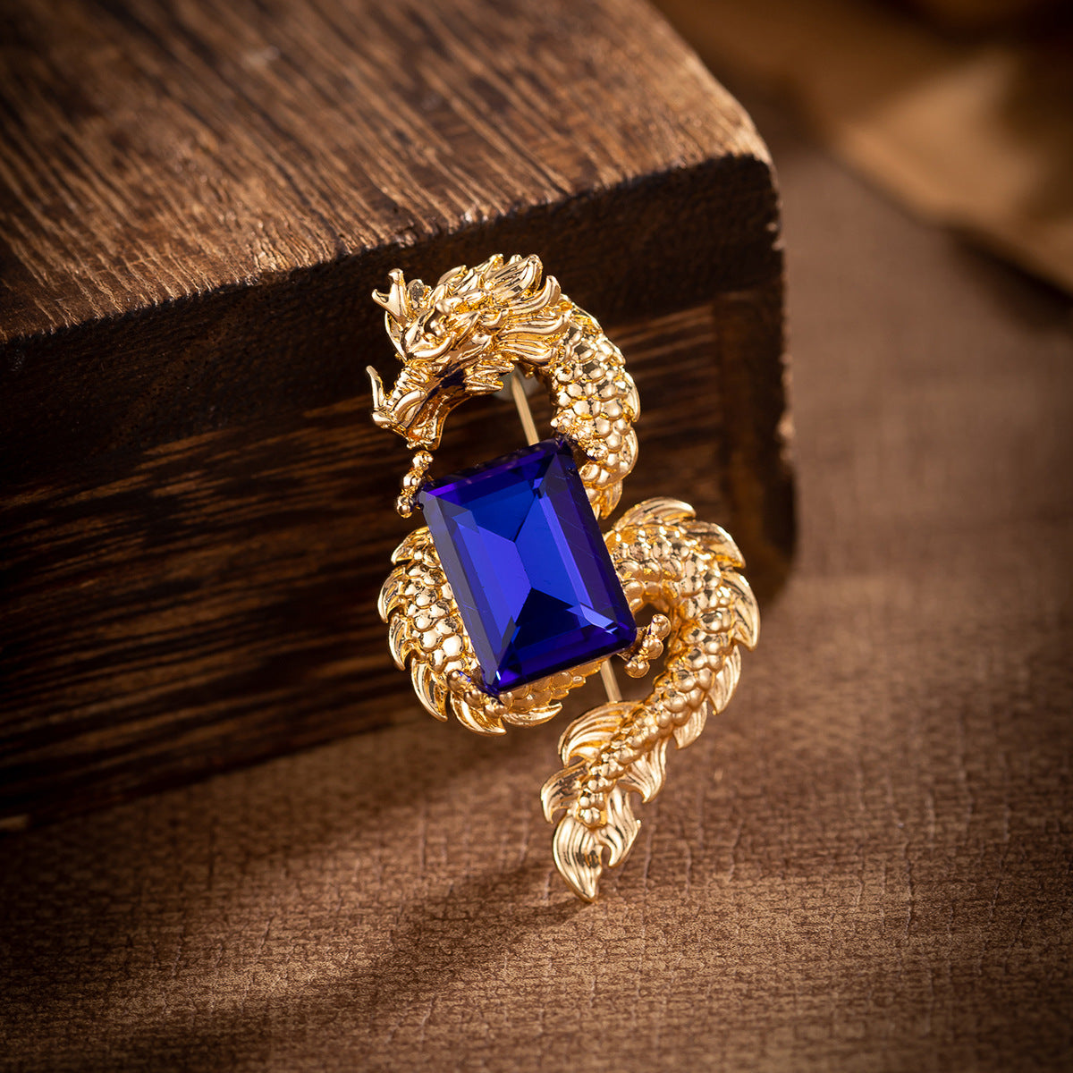 Close-up gold dragon brooch with faceted rectangular blue crystal centerpiece