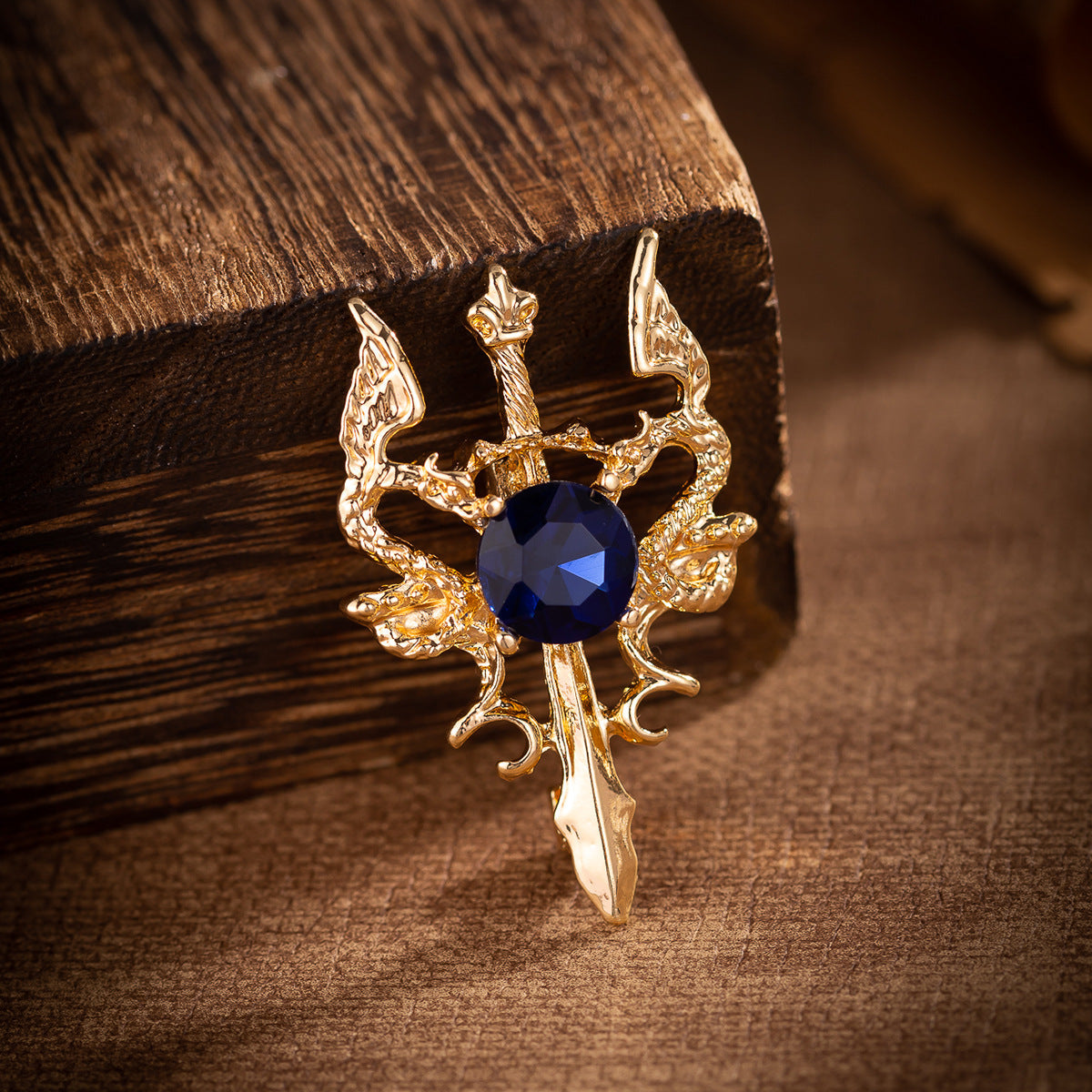 Gold double dragon sword brooch close-up with dark blue round gemstone