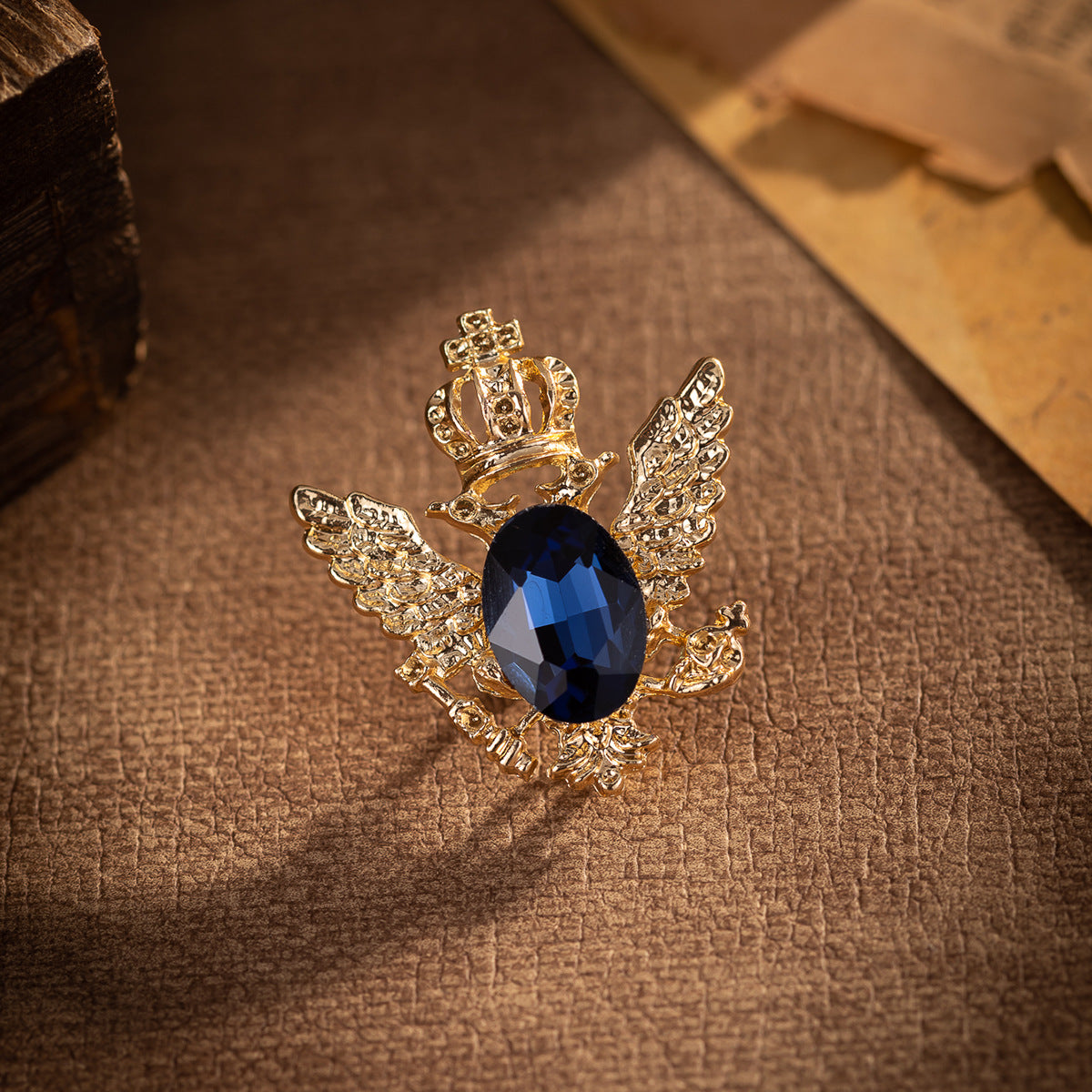 Gold winged eagle lapel pin with crown and dark blue oval crystal centerpiece