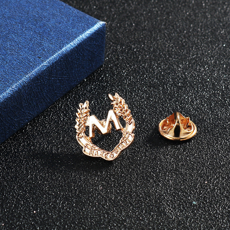 Gold M wheat ear brooch with pin backing, close-up side view