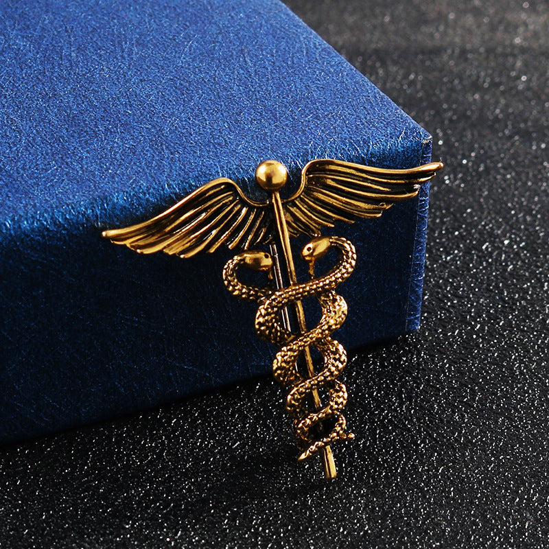 Gold angel wings and snake caduceus brooch pin on blue fabric
