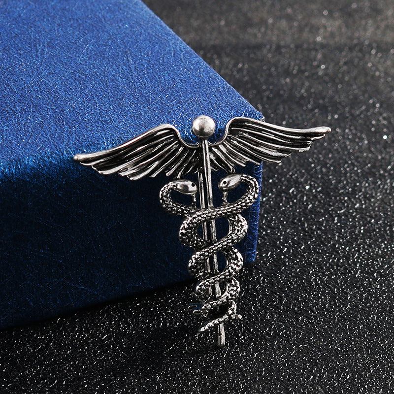 Silver angel wings and snake caduceus brooch pin on blue fabric