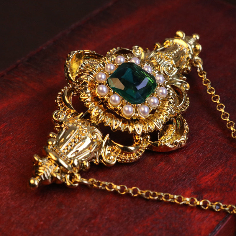 Emerald-green crystal brooch with ornate filigree, round pearls and linked chain tassel