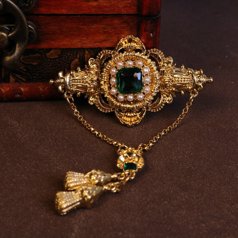 Gold-tone brooch centerpiece with emerald-green stone, pearl trim and dangling chain