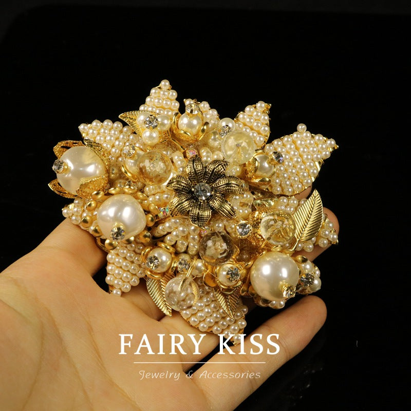 Beaded flower brooch in gold tones with faux pearls, leaf details, and rhinestone center.