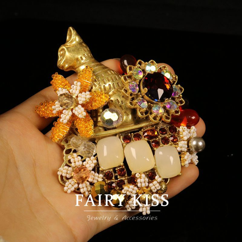 Cat-shaped brooch held in hand; multicolor gems, faux pearls, and cream square cabochons