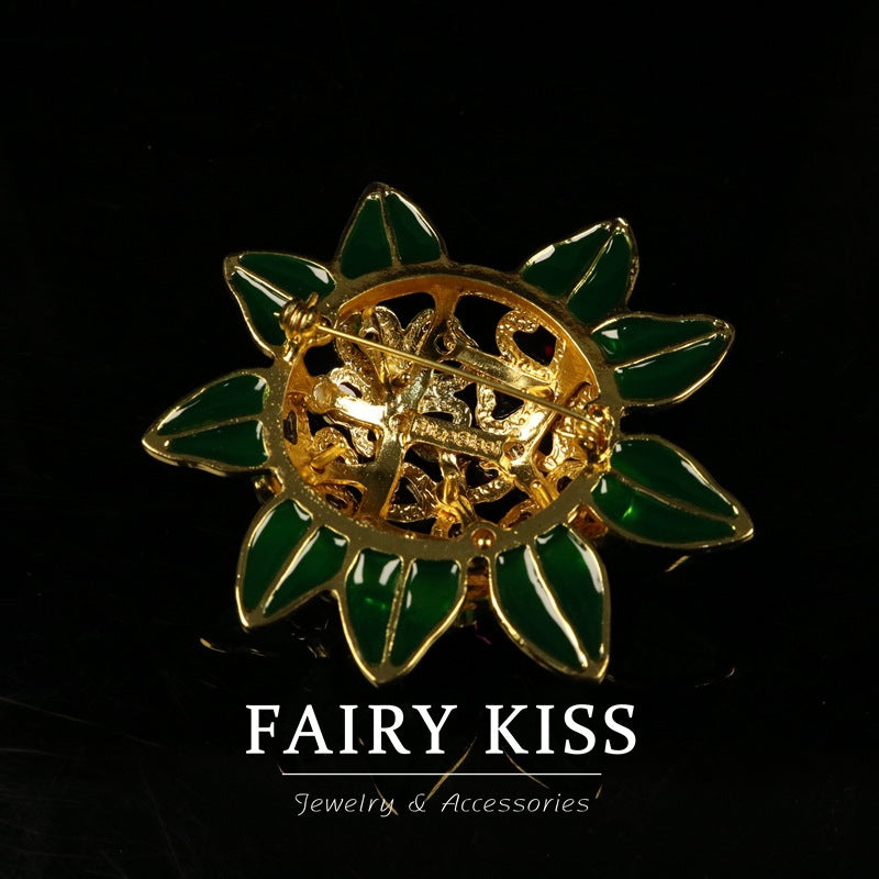 Gold-backed enamel flower brooch with green leaf petals and red/purple gem stones