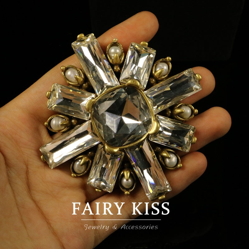 Rhinestone brooch in hand: clear central crystal with gold-toned burst surround