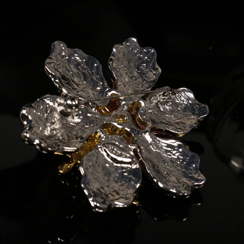 Floral rhinestone brooch side view with silver-tone petals, gold leaves, blue center
