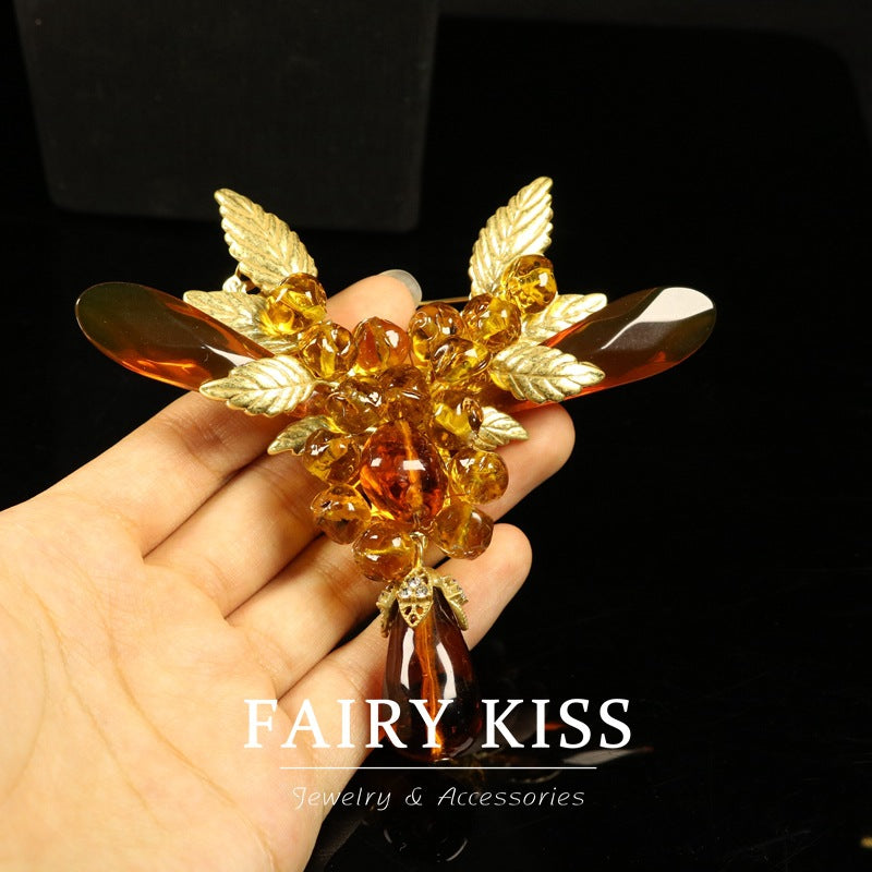 Amber bead wing brooch with gold-tone setting, held in hand for size