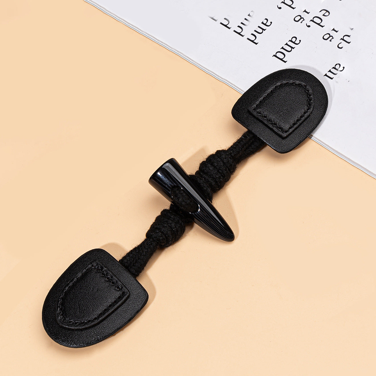 Black leather sew-on button with resin horn spike and braided cord, close-up