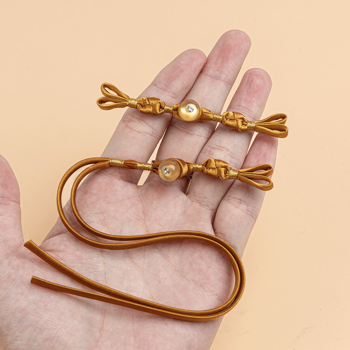 Goldfarbene geflochtene Zierknöpfe mit runder Stein-Perle und Schleife, in Handfläche
