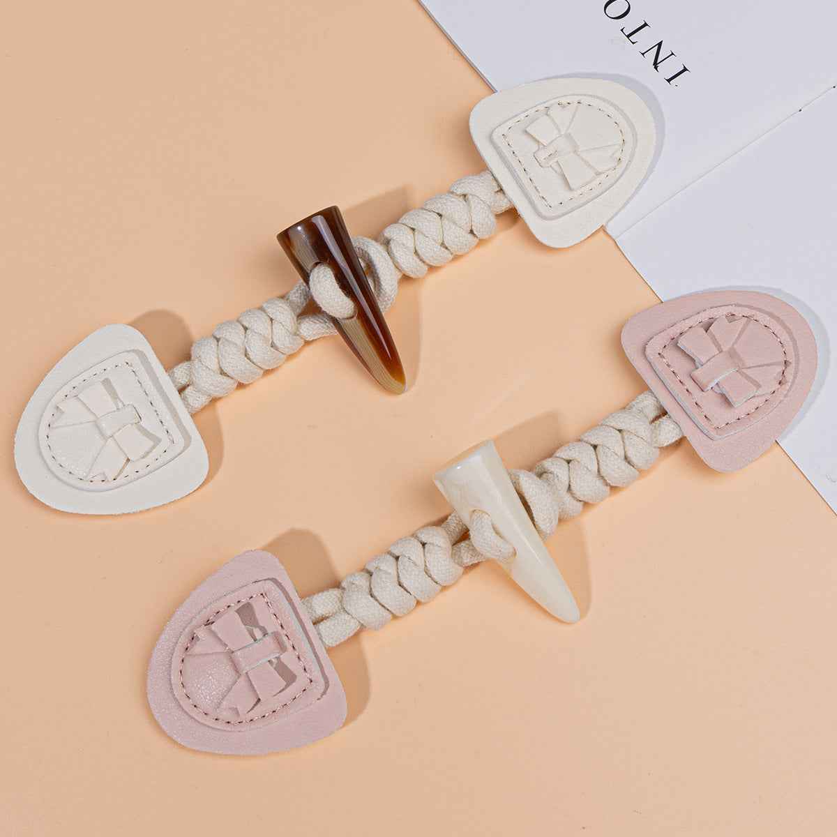 Children’s coat buckles in beige and pink with braided cords and horn-shaped connectors