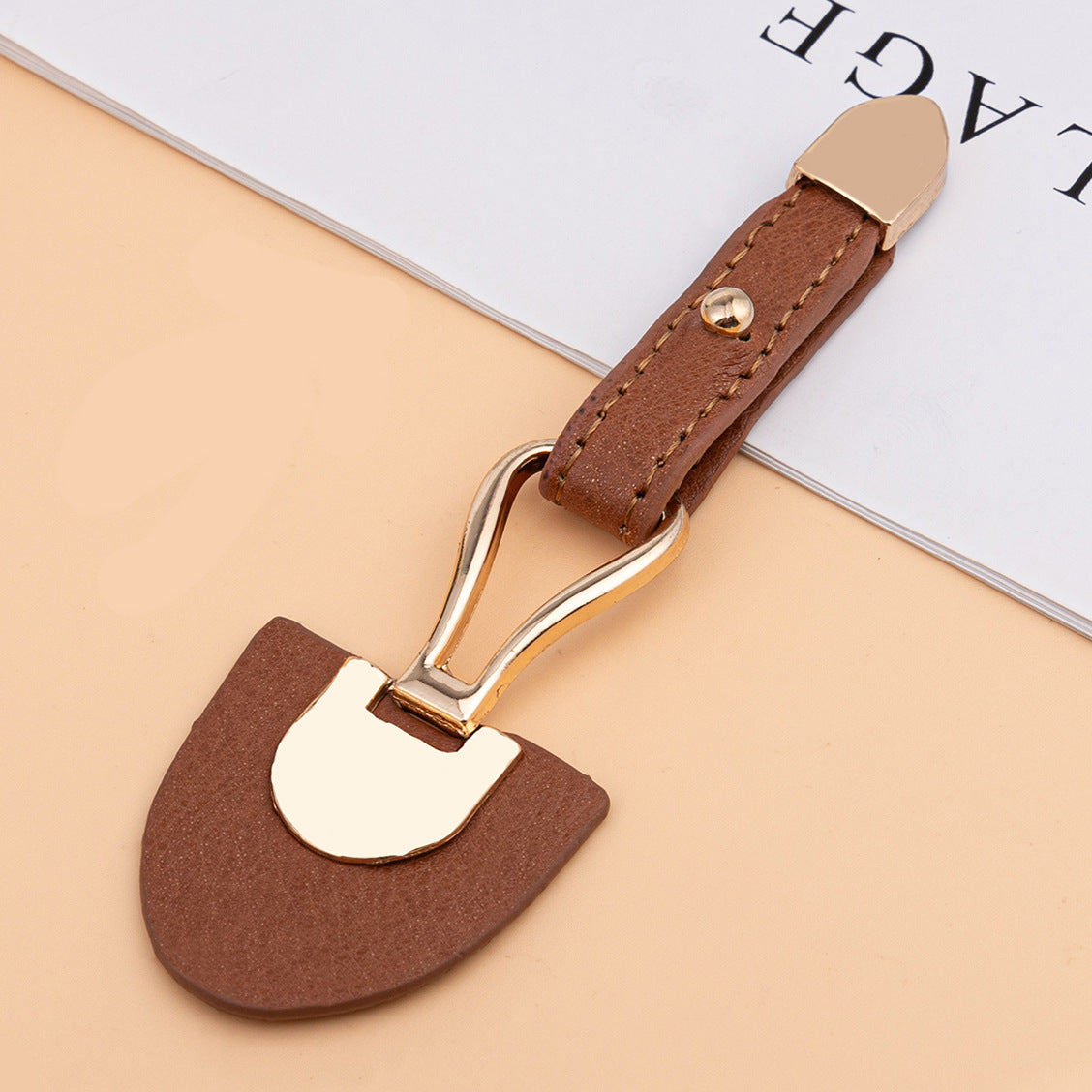 Brown leather sew-on toggle with gold metal buckle and visible stitching