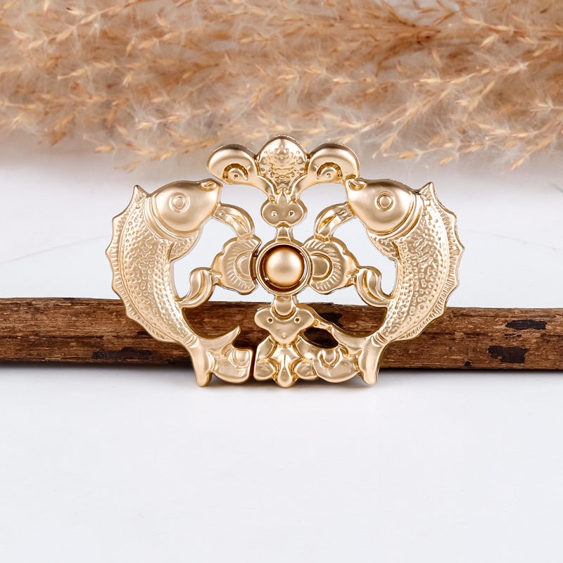 Gold-tone carp frog button close view with scalloped frame and round center bead