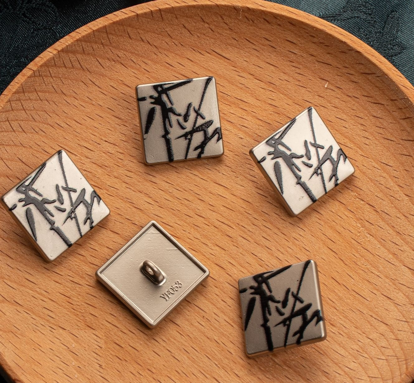 Square buttons with white faces and black ink bamboo-style motif on wooden board