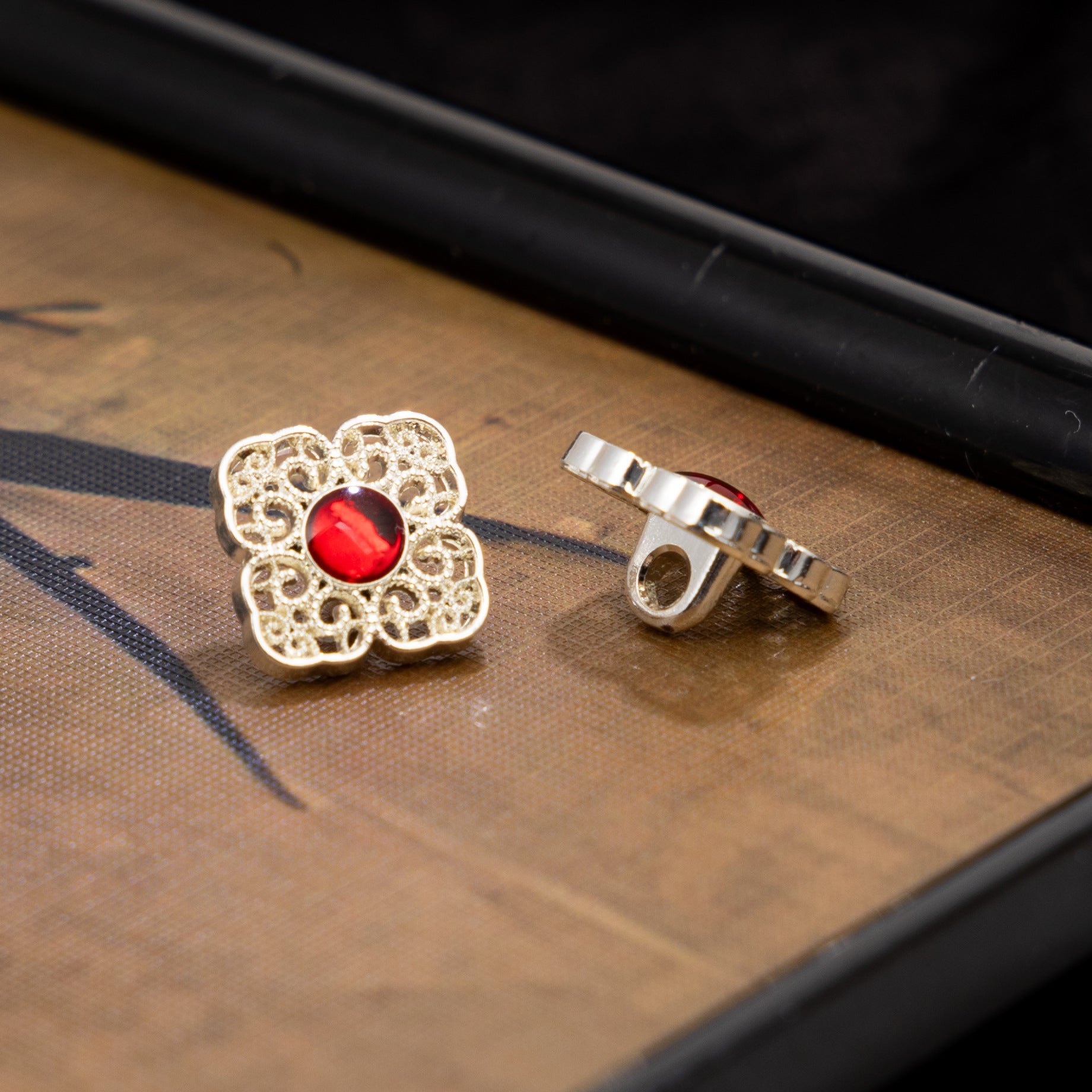 Silver square button with red round center and metal back, ornate filigree