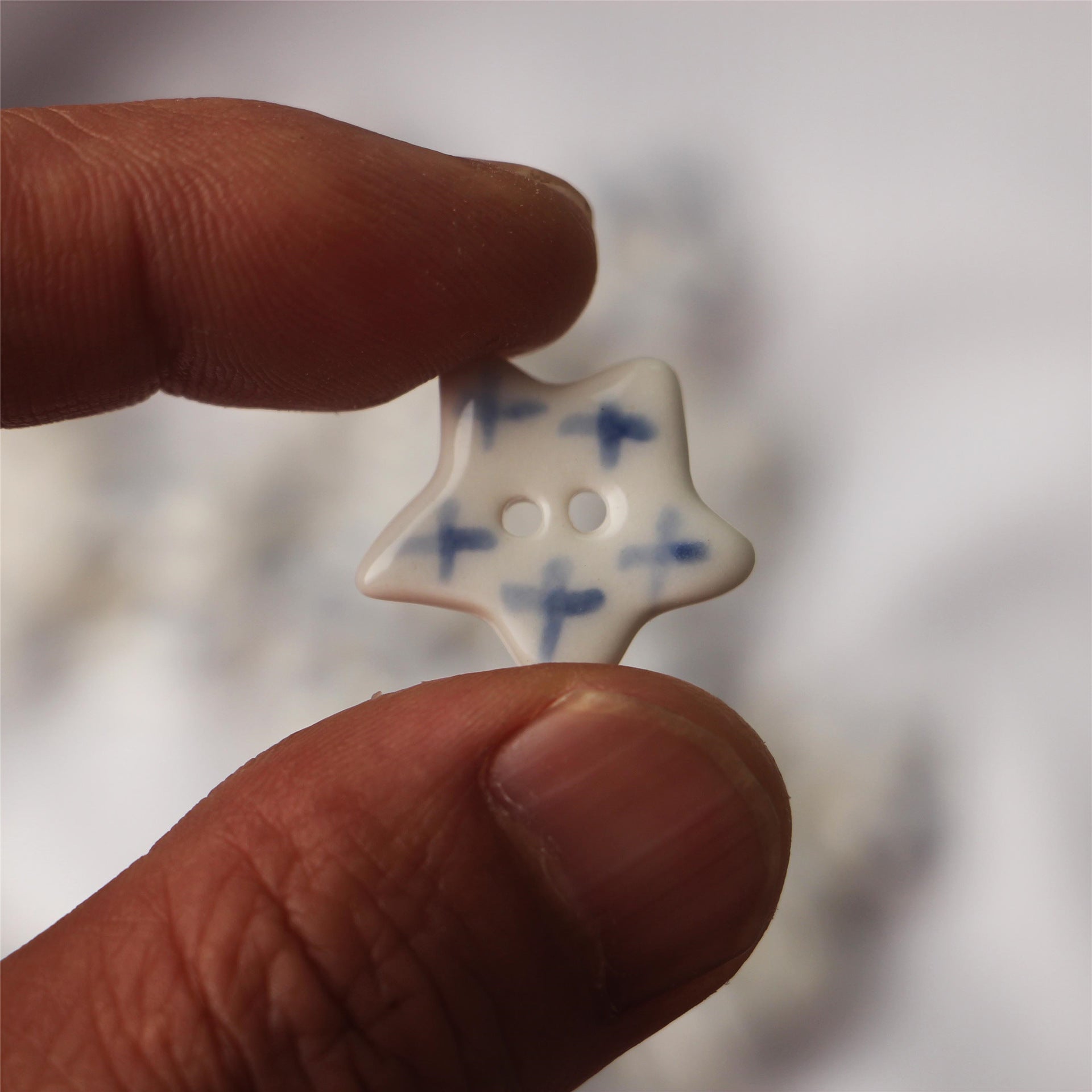 Hand holding a blue-and-white five-point star ceramic button with two holes