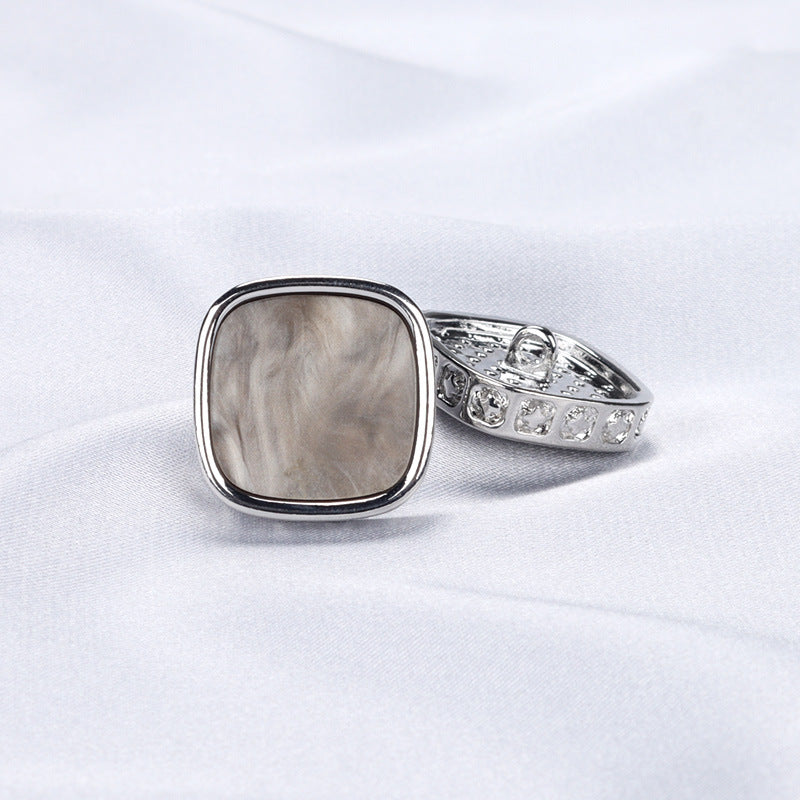 Silver metal shank coat button, square face, patterned border, side view