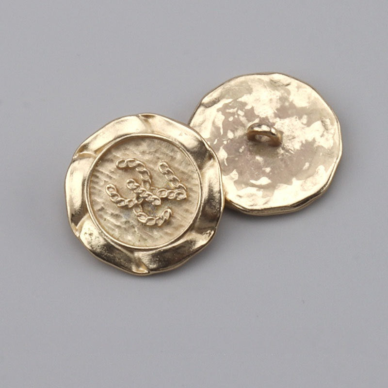 Gold metal button with shank back, ornate engraving on front
