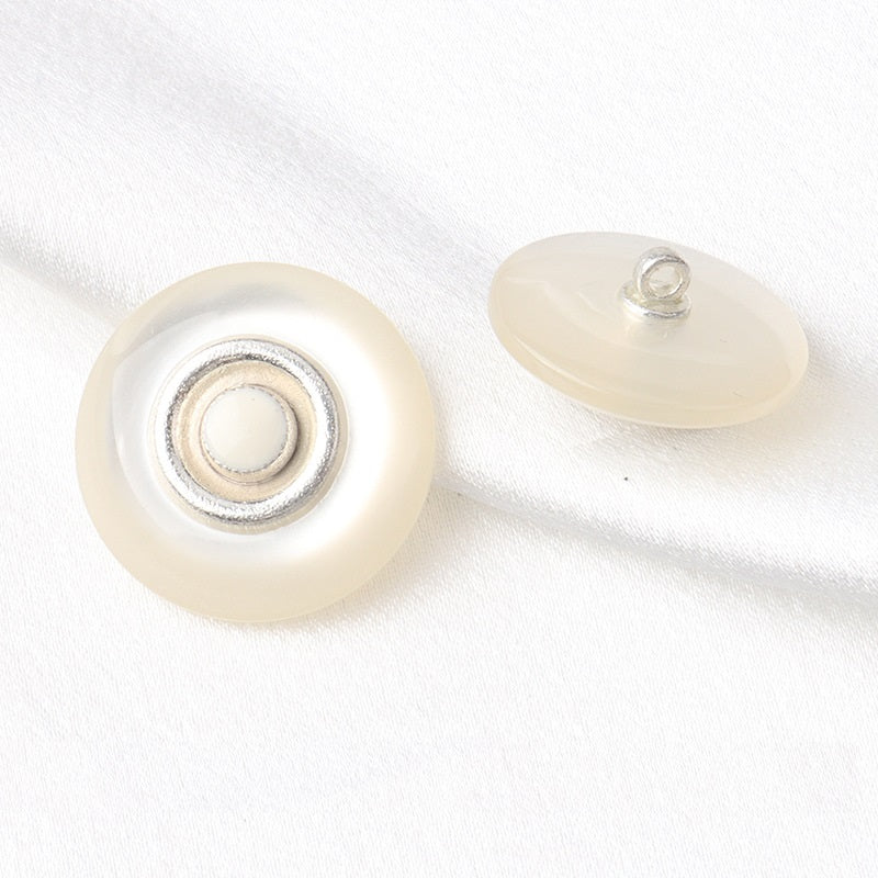 Round coat button, two-tone pearl resin front with silver rim; back shows metal shank