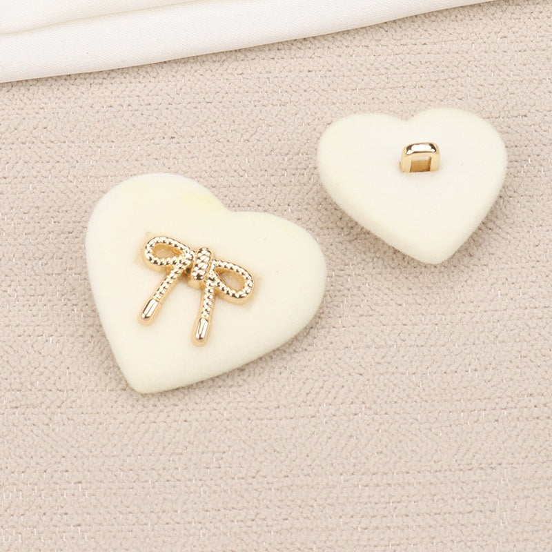 White heart-shaped velvet shank button with rhinestone bow and two metal prongs