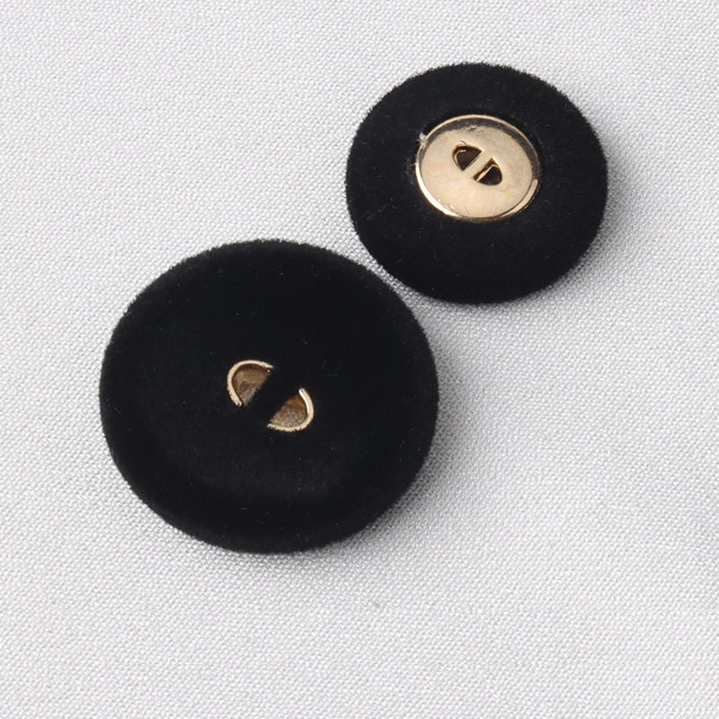 Two black flocked coat buttons, round face with two gold-tone holes