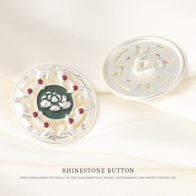 Two-piece view of round rhinestone button: front with green floral center and red stones, back metal