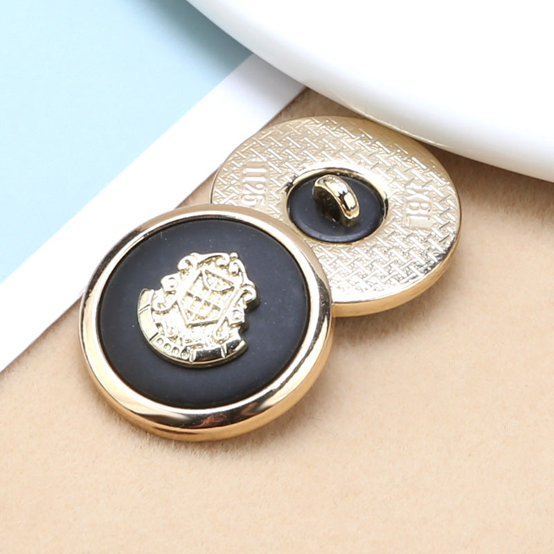 Two round buttons close-up: black resin front with gold anchor-shield crest, gold rim details