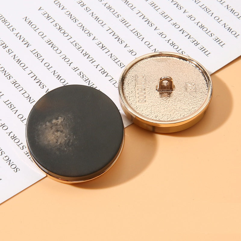 Black round resin shank button front with beige metal back, gold rim