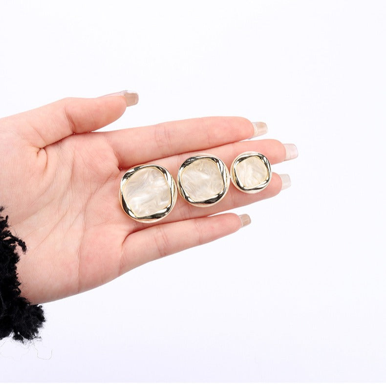 Beige resin buttons, round metal shank backs, held in hand
