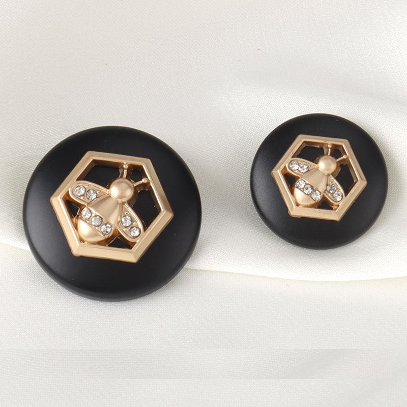 Two round black metal buttons with gold bee hex motif and clear rhinestones