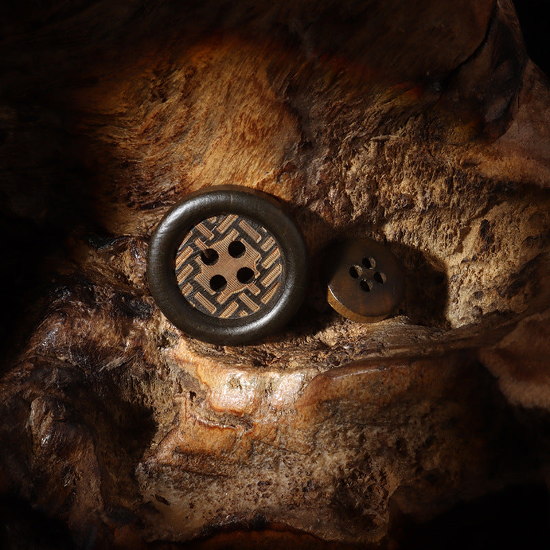 Two dark brown 4-hole wood buttons with laser-engraved motif on textured surface