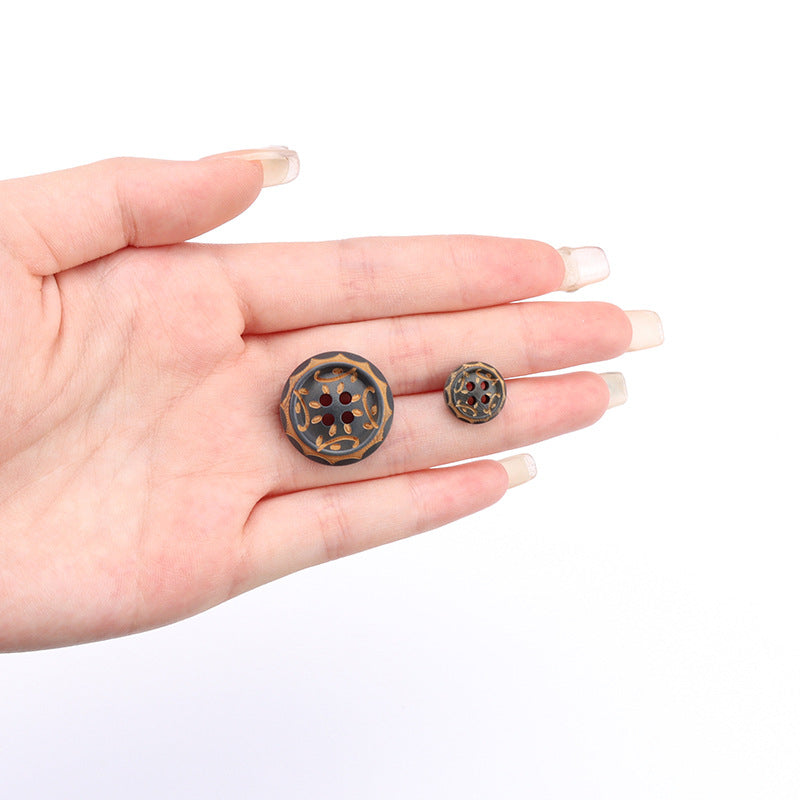 Gray-brown four-hole wood button with ornate gold pattern, shown in hand