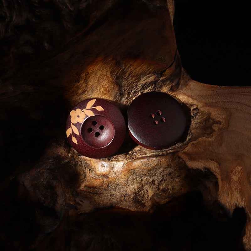 Zwei rotbraune Holzknöpfe mit Blattblumenmotiv, 4-Loch-Ansicht