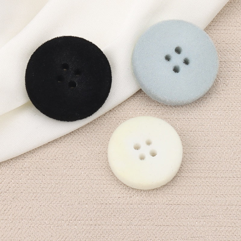 Flocked flat buttons in black, light blue, and white, each with four holes (15–25mm)