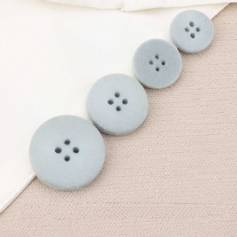 Light blue flocked flat buttons with four holes, 15–25mm set on fabric