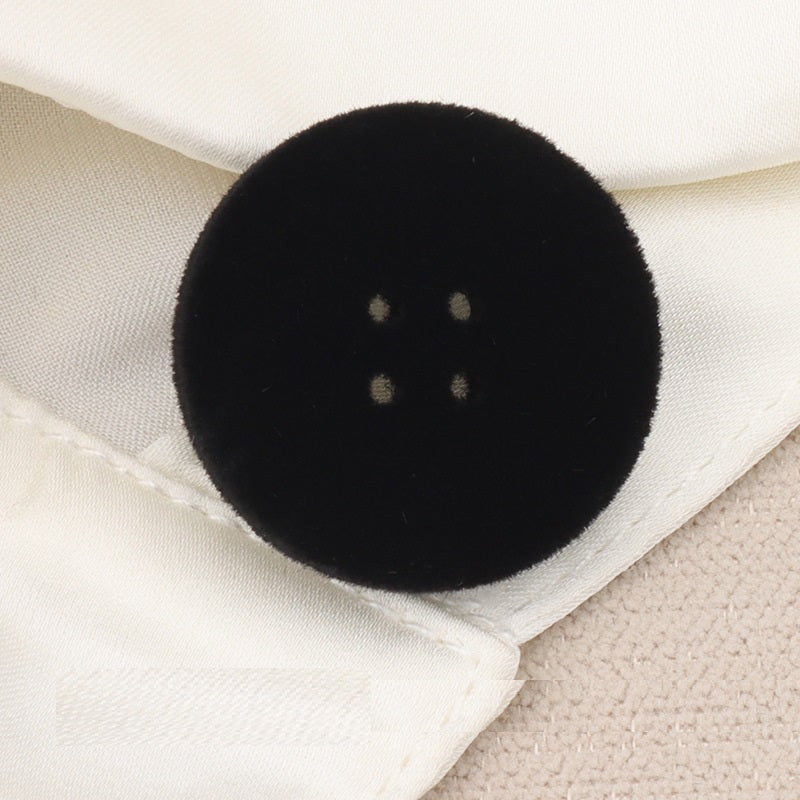 Black flocked four-hole flat button (15–25mm), close-up with fabric backdrop