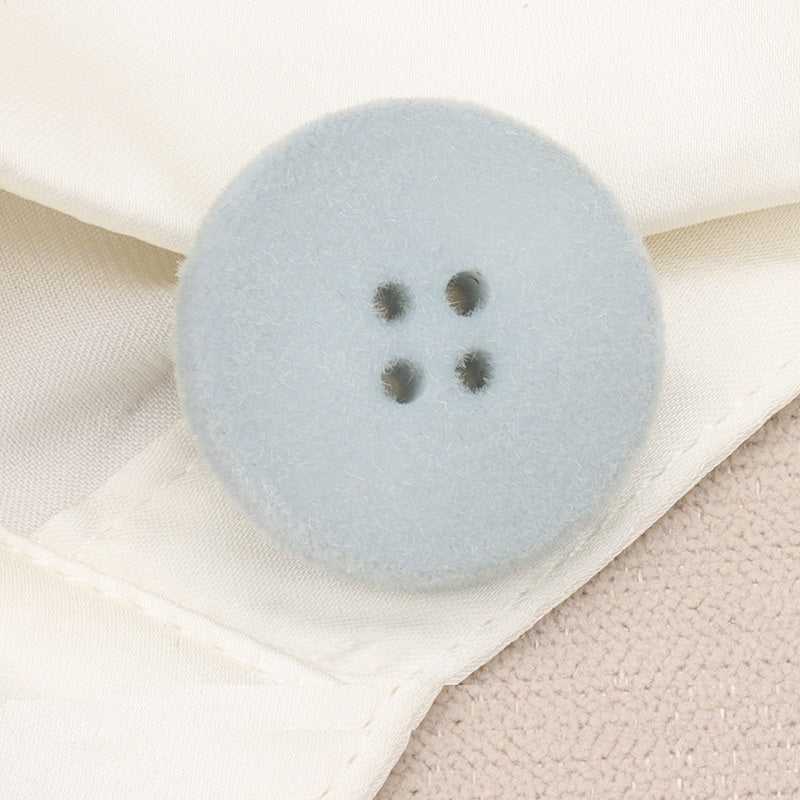 Light blue flocked flat button with four holes, 15–25mm, close-up on fabric